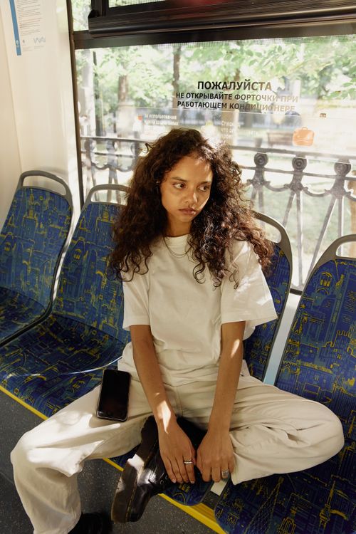 Free A young woman with curly hair sits pensively in a sunlit public transportation seat. Stock Photo