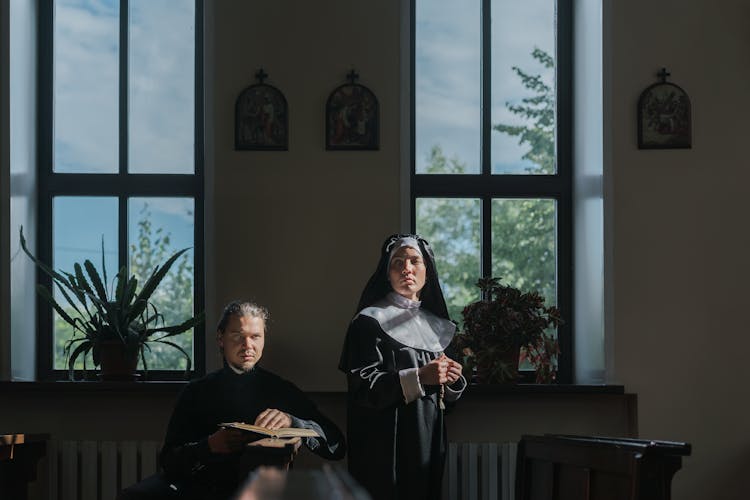 Nun Standing Beside A Priest Sitting On Church Pew