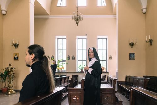 Free A nun standing in a serene church setting with sunlight streaming through large windows. Stock Photo