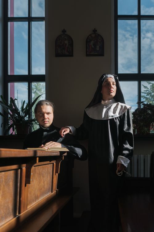 Free Priest and nun in prayer at a sunlit church altar with stained glass windows. Stock Photo