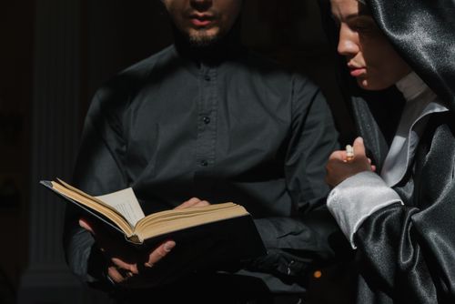 Free Priest and nun together studying a religious book, focusing on devotion and faith. Stock Photo
