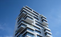 低角度镜头捕捉到一栋引人注目的现代公寓，其独特的阳台设计与清澈的蓝天相映成趣