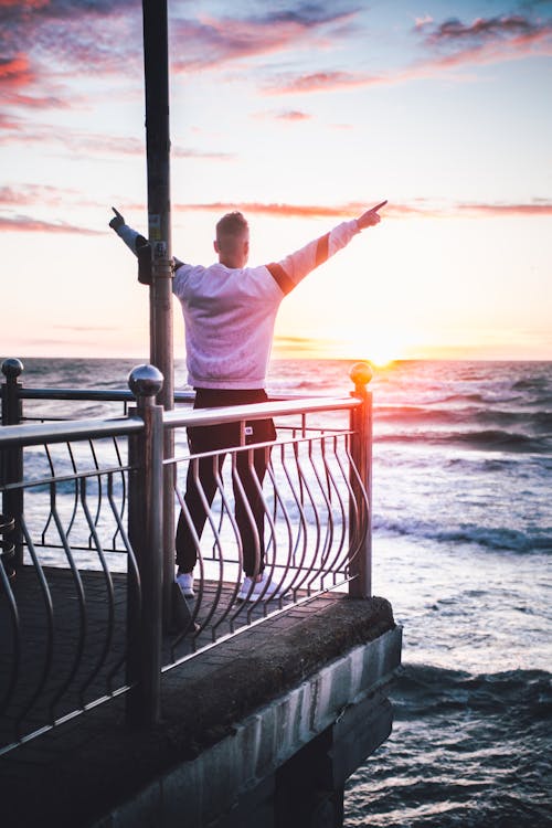A Man Standing on a Balcony Above the Sea Watching the Sunset