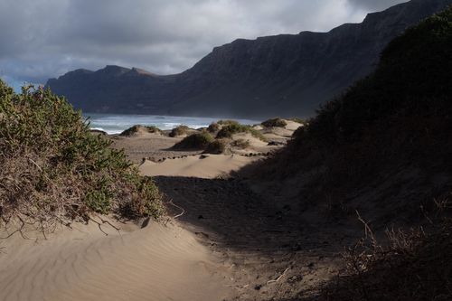 Free Scenic view of a sandy coastline with dunes and a rugged hillside under a cloudy sky. Stock Photo