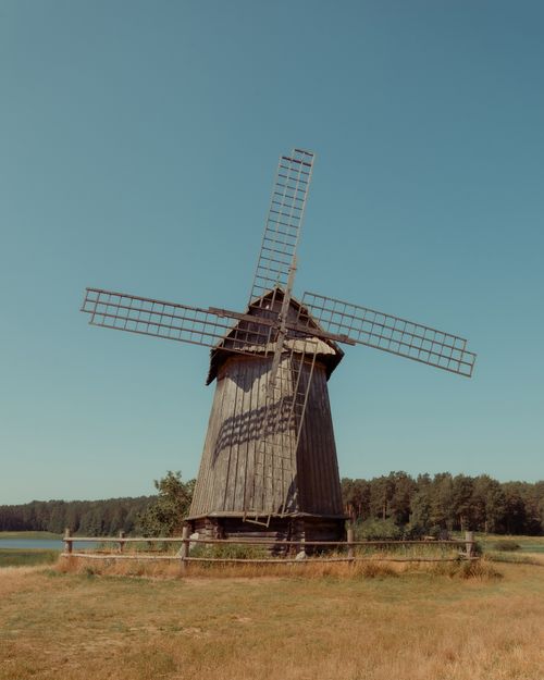 Free A rustic wooden windmill stands tall in the scenic countryside of Pskov, Russia under a clear blue sky. Stock Photo