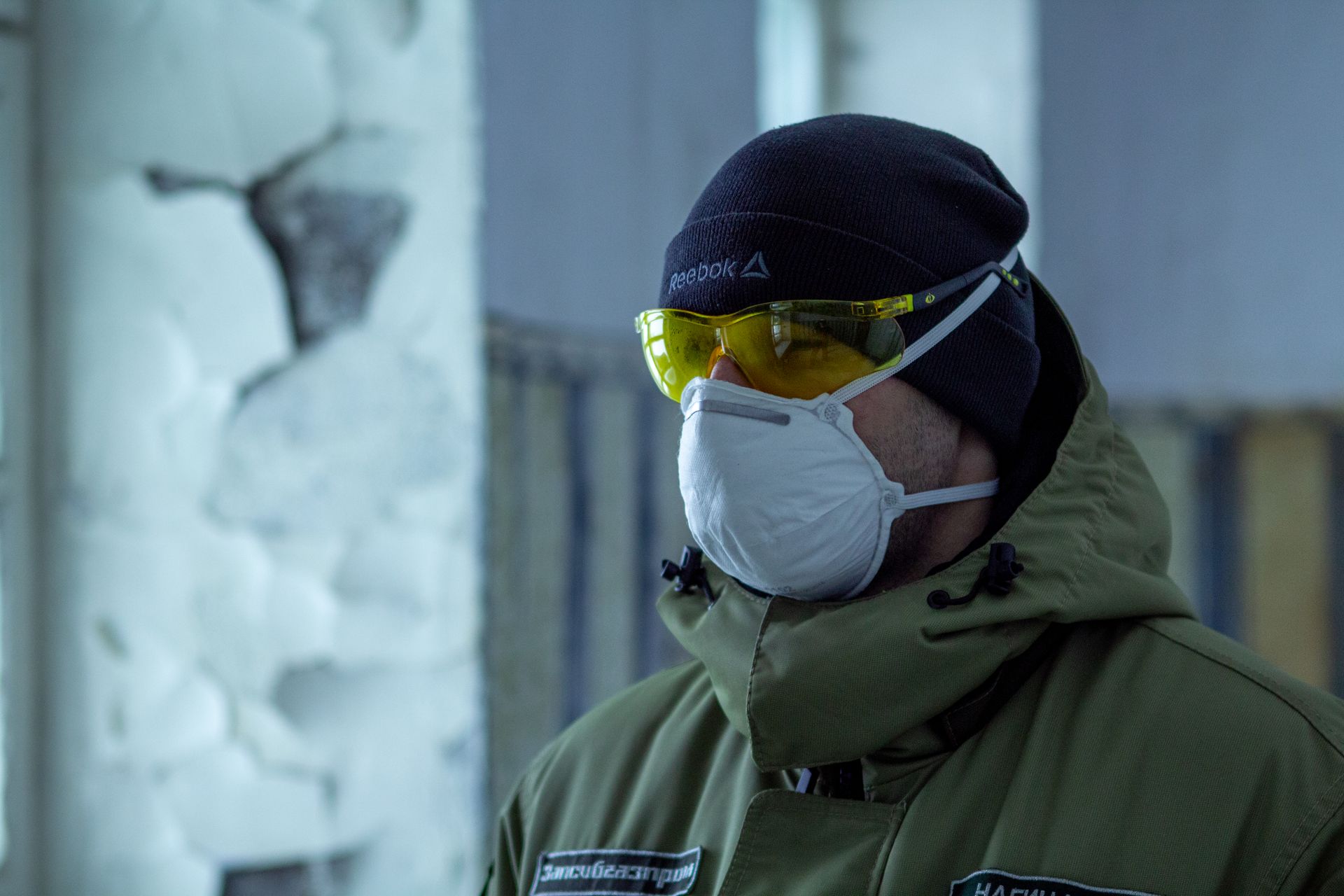 Man wearing safety glasses and mask indoors, emphasizing health and safety measures.