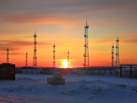 Industrial utility poles silhouetted against a vibrant sunset in a snowy landscape.