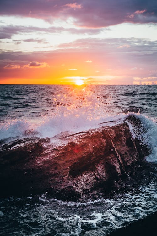 Free Waves Breaking on a Rocky Shore at Sunset  Stock Photo