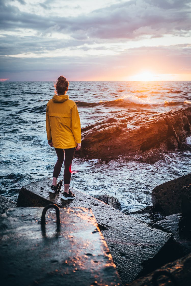 Woman Standing On Wave Breakers By Sea Shore