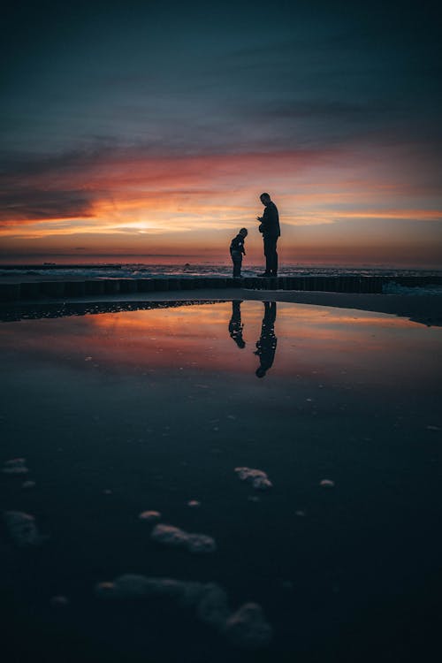 Free Man and a Boy Standing on Beach at Sunset Stock Photo