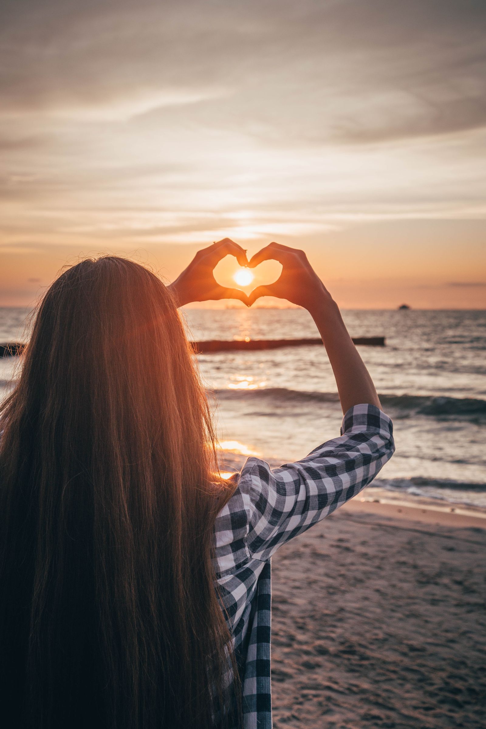 Woman forming a heart shape with her hands during sunset on the beach