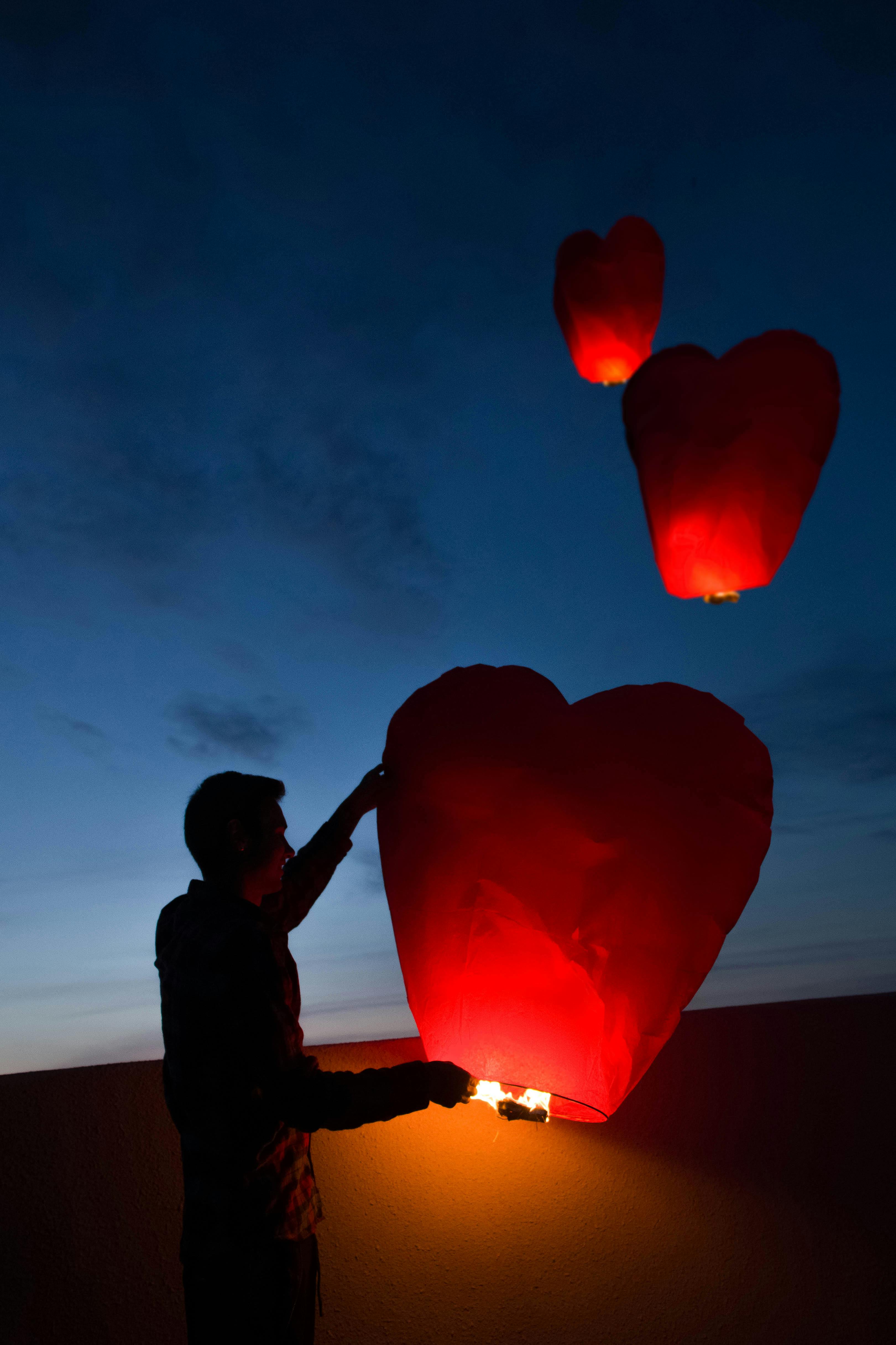 在暮色的天空下，一个男人的剪影发射出红色的心形灯笼，象征着爱与庆祝