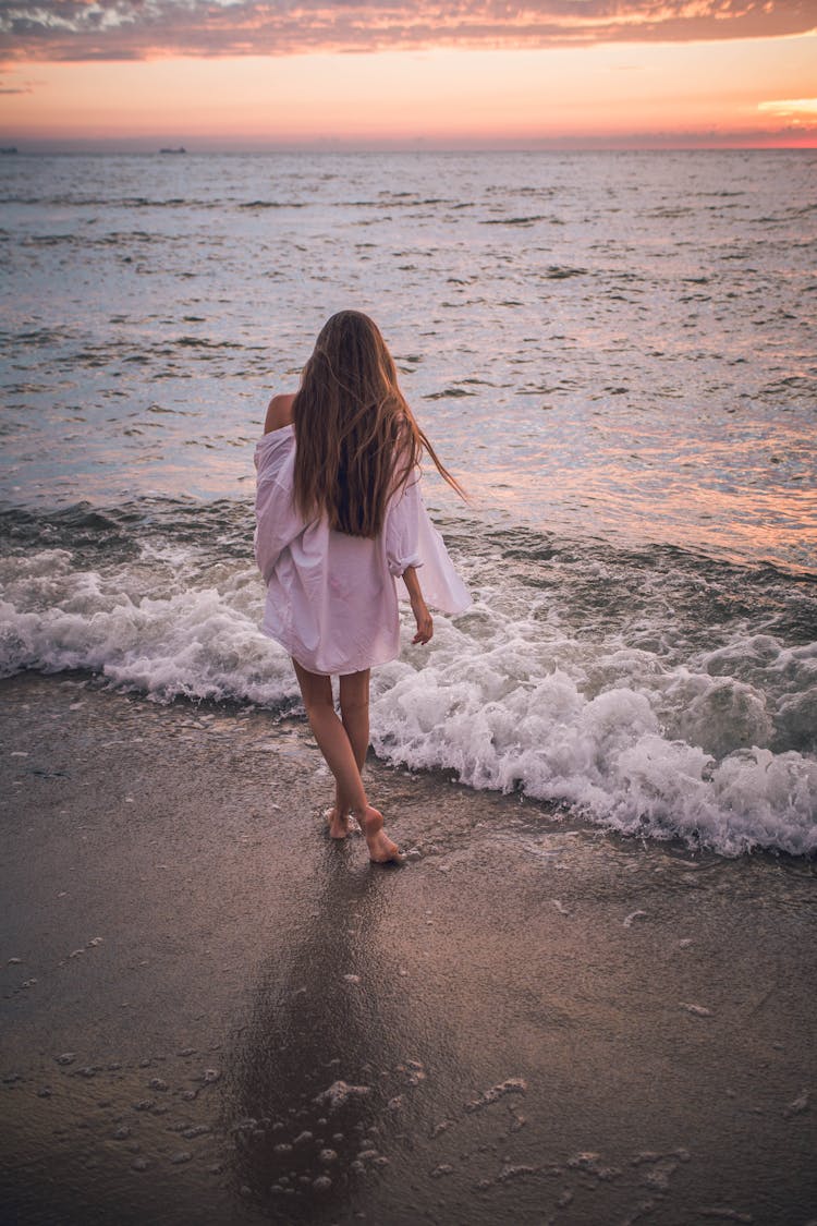 Woman Walking Along Beach At Sunset