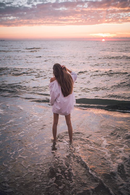 A Woman in White Long Sleeves Shirt Standing on Beach Shore