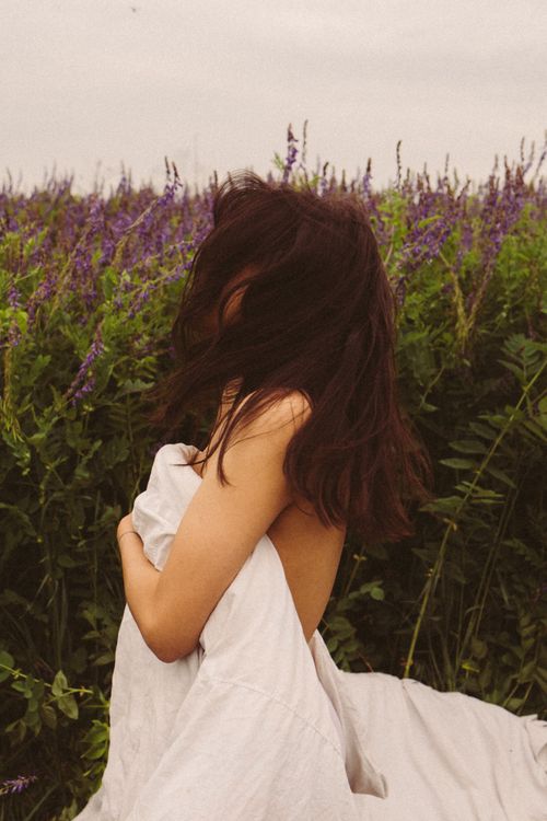 Free A woman with long hair and fabric posing in a serene, flower-filled meadow. Stock Photo