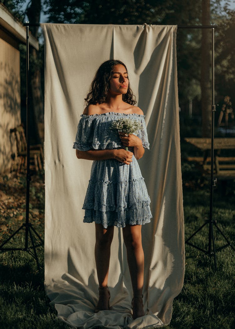 Woman Wearing Blue Summer Dress Posing With A Bouquet Against White Drape Outdoors