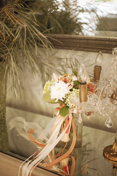 Bouquet of Flowers in Glass Vase Decorated with Ribbons Beside Table Lamp