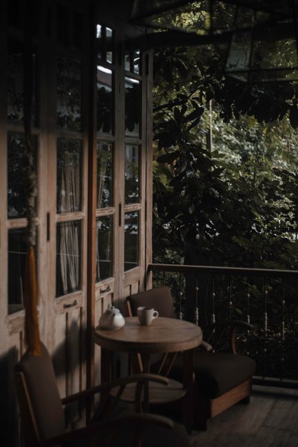 A serene vintage patio with wooden chairs and a round table surrounded by lush greenery.
