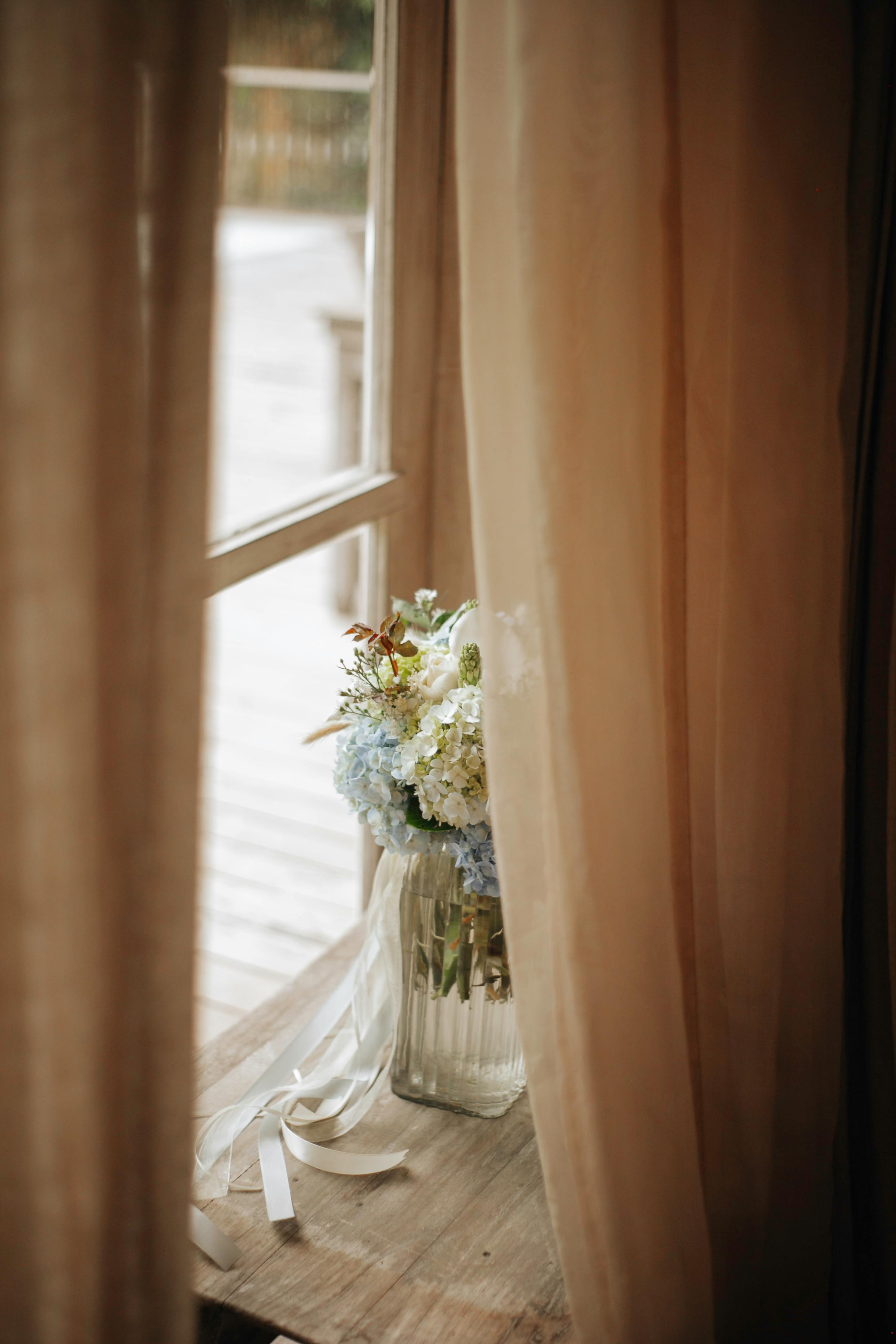 Charming bouquet on a wooden sill framed by flowing curtains, exuding elegance and rustic charm.