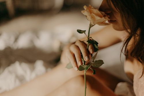Free A serene close-up of a woman gently holding and smelling a rose in soft lighting. Stock Photo
