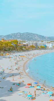 Aerial shot of a bustling coastal city beach with tourists enjoying summer under clear skies.