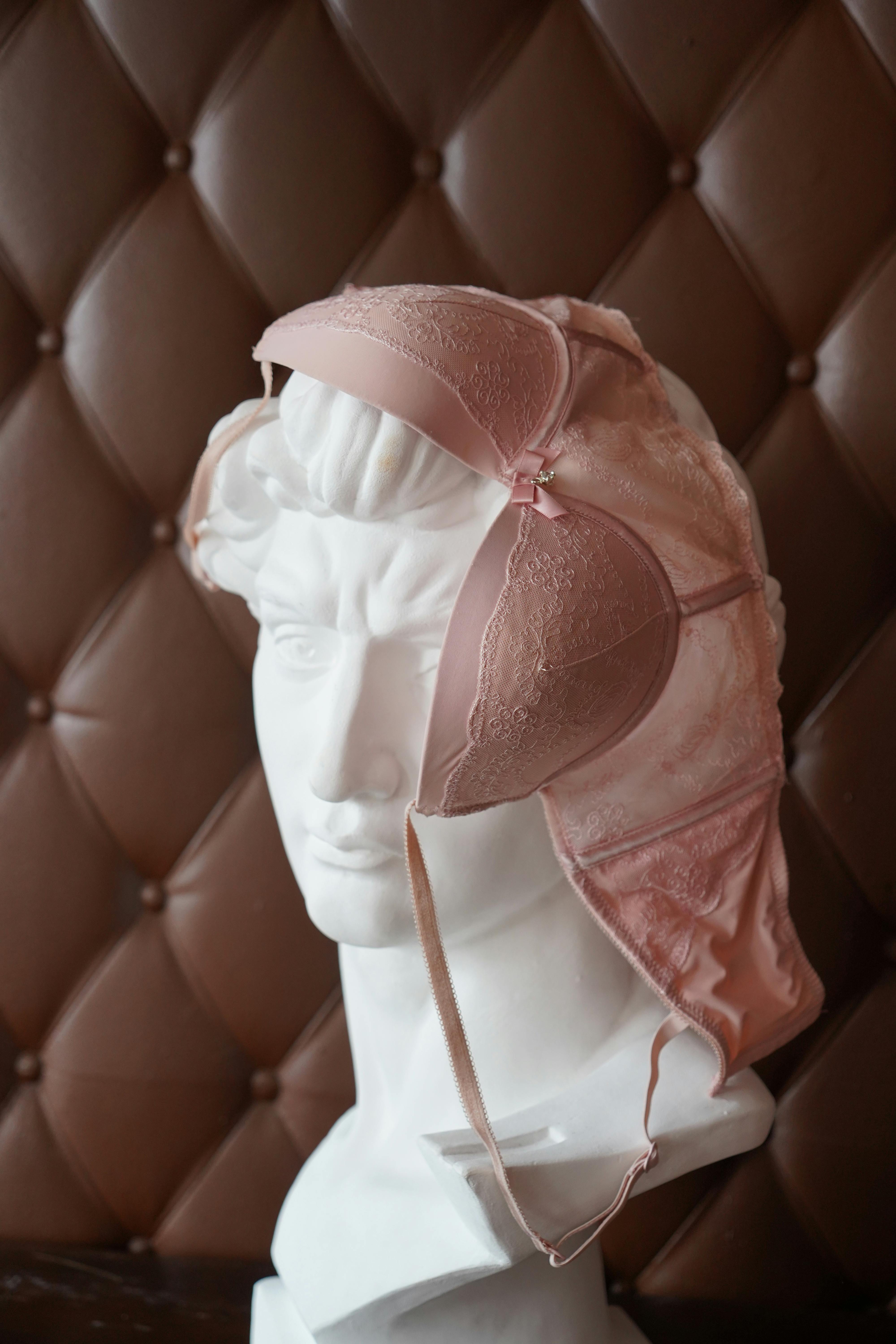 A marble bust adorned with a pink bra resting on a classic leather sofa.
