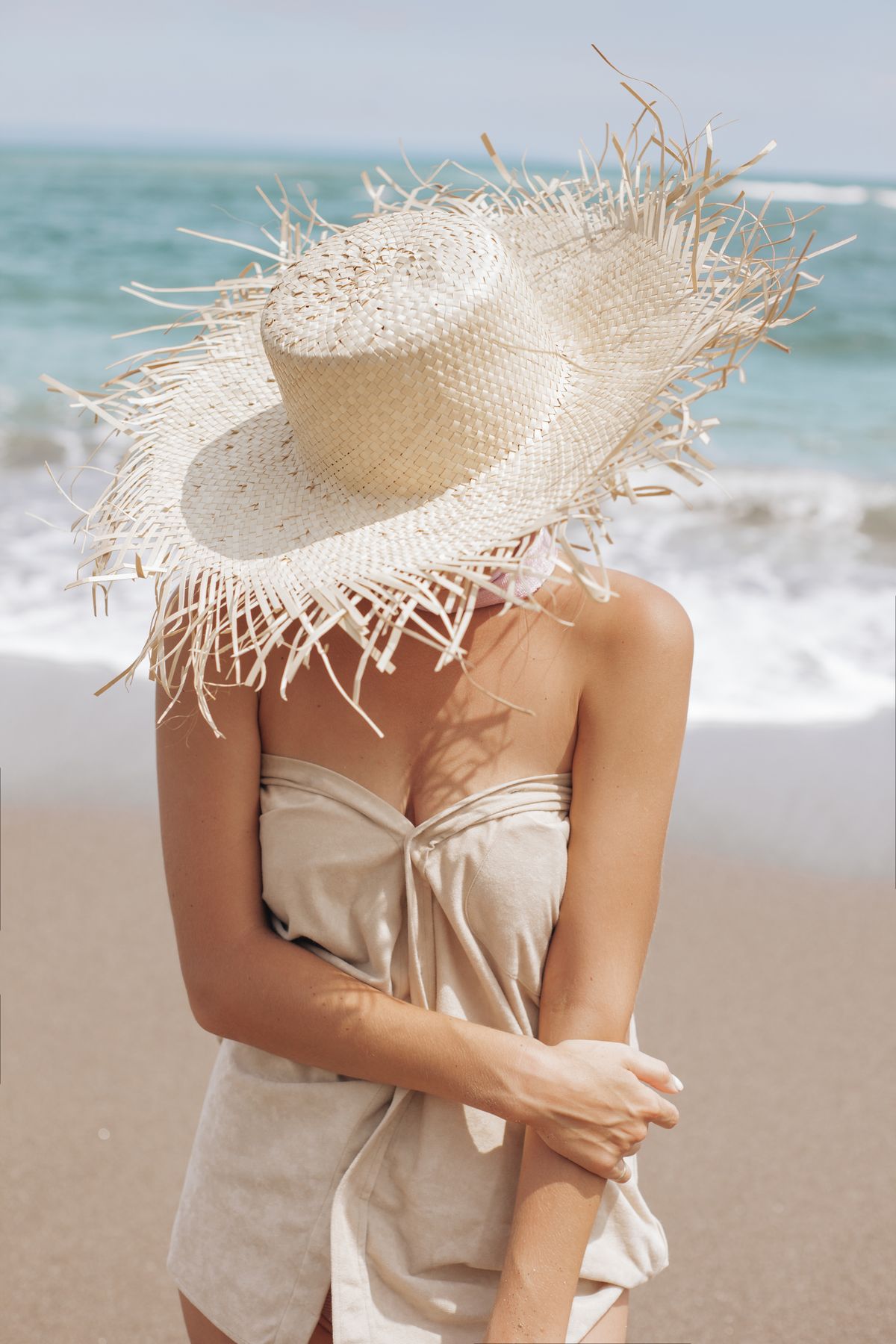 A woman with a straw hat covering her face — the straw hat, the finishing piece of a European summer wardrobe