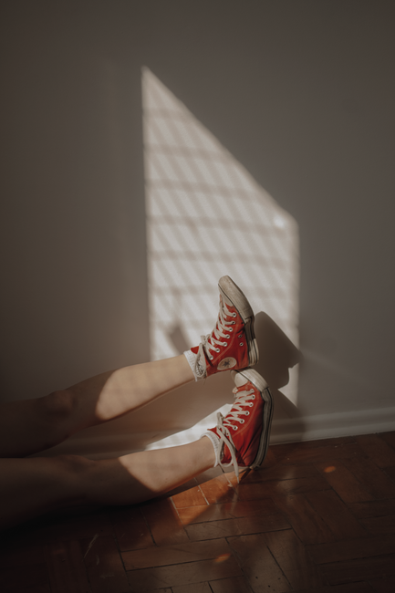Relaxed scene featuring red sneakers resting on a sunlit wooden floor, creating a cozy mood.