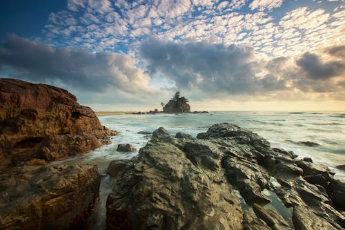 Gratis Batuan Coklat Di Tepi Laut Di Bawah Langit Awan Putih Foto Stok