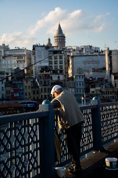 A man leans over Galata Bridge while fishing, with Galata Tower visible in the background.
