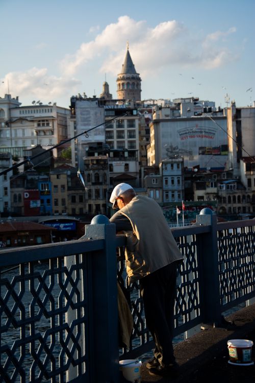 Free A man leans over Galata Bridge while fishing, with Galata Tower visible in the background. Stock Photo