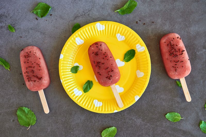 Strawberry ice pops on a vibrant yellow plate with mint leaves