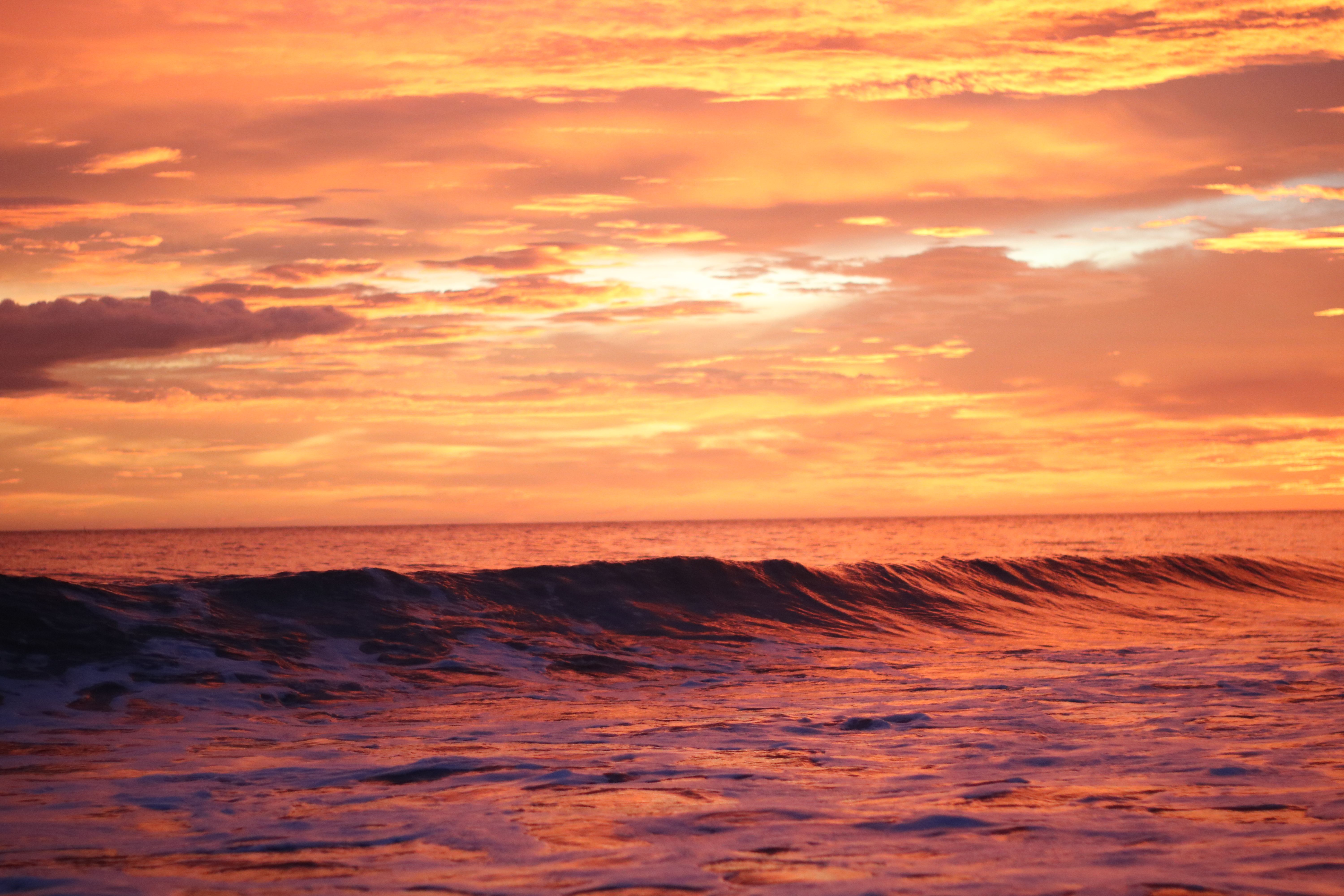 Stunning ocean sunset scene with vibrant clouds and dramatic waves, capturing nature's beauty.