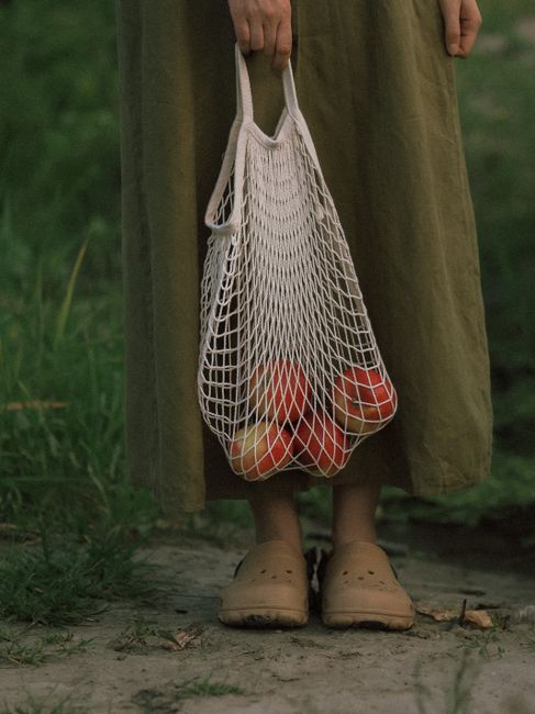 A person holding a reusable net bag filled with apples, showcasing sustainability and eco-friendly living.