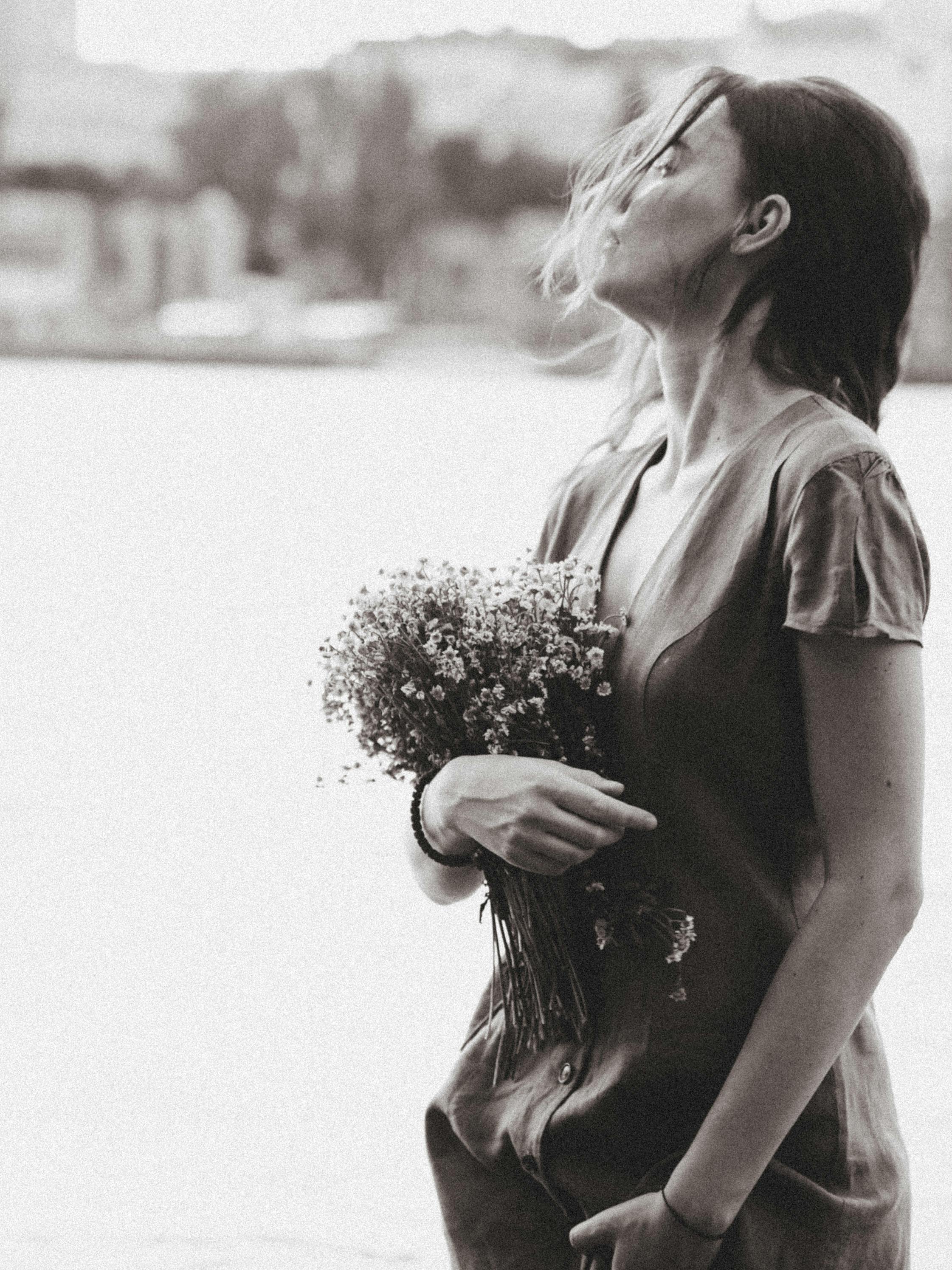 A serene woman holding a bouquet by the water in a monochrome setting.