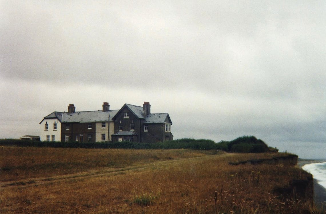 An Old House Standing On A Cliff Near Coast Under Gray Sky