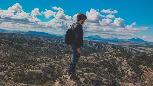 Man Wearing Blue Jeans Standing on Gray Stone Fragment Under Cloudy Sky