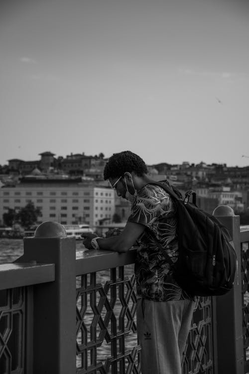  Man with Backpack Standing Beside a Fence Near a Lake