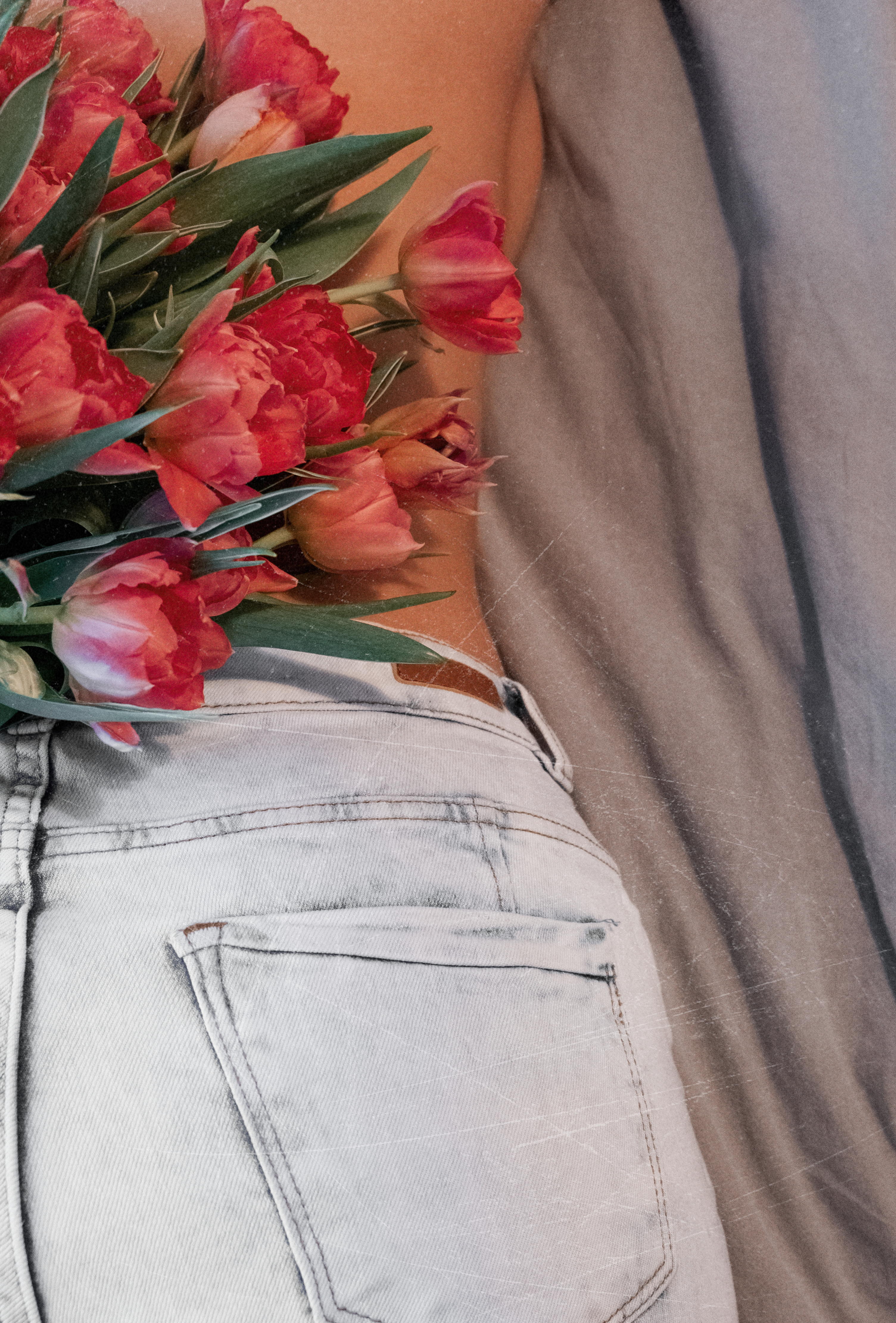Artistic shot of a woman holding tulips in her back pocket, emphasizing femininity and romance.
