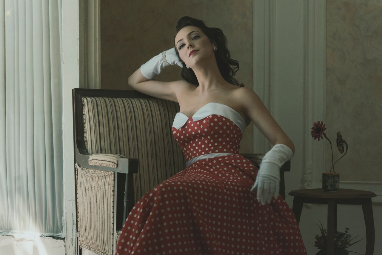 a woman in a vintage polka dot dress poses elegantly indoors with a cl
