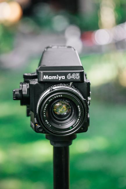 Close-up of a vintage Mamiya 645 camera on a tripod in an outdoor setting.