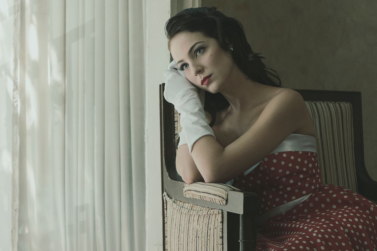 elegant woman in a red polka dot dress sits thoughtfully indoors in a