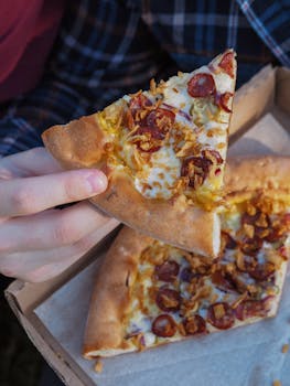 A close-up shot of a pepperoni pizza slice being held, showcasing melted cheese and crunchy toppings.