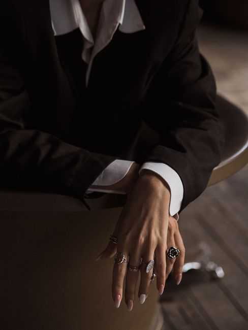 Stylish fashion shot featuring black coat and rings with elegant pose in moody lighting.