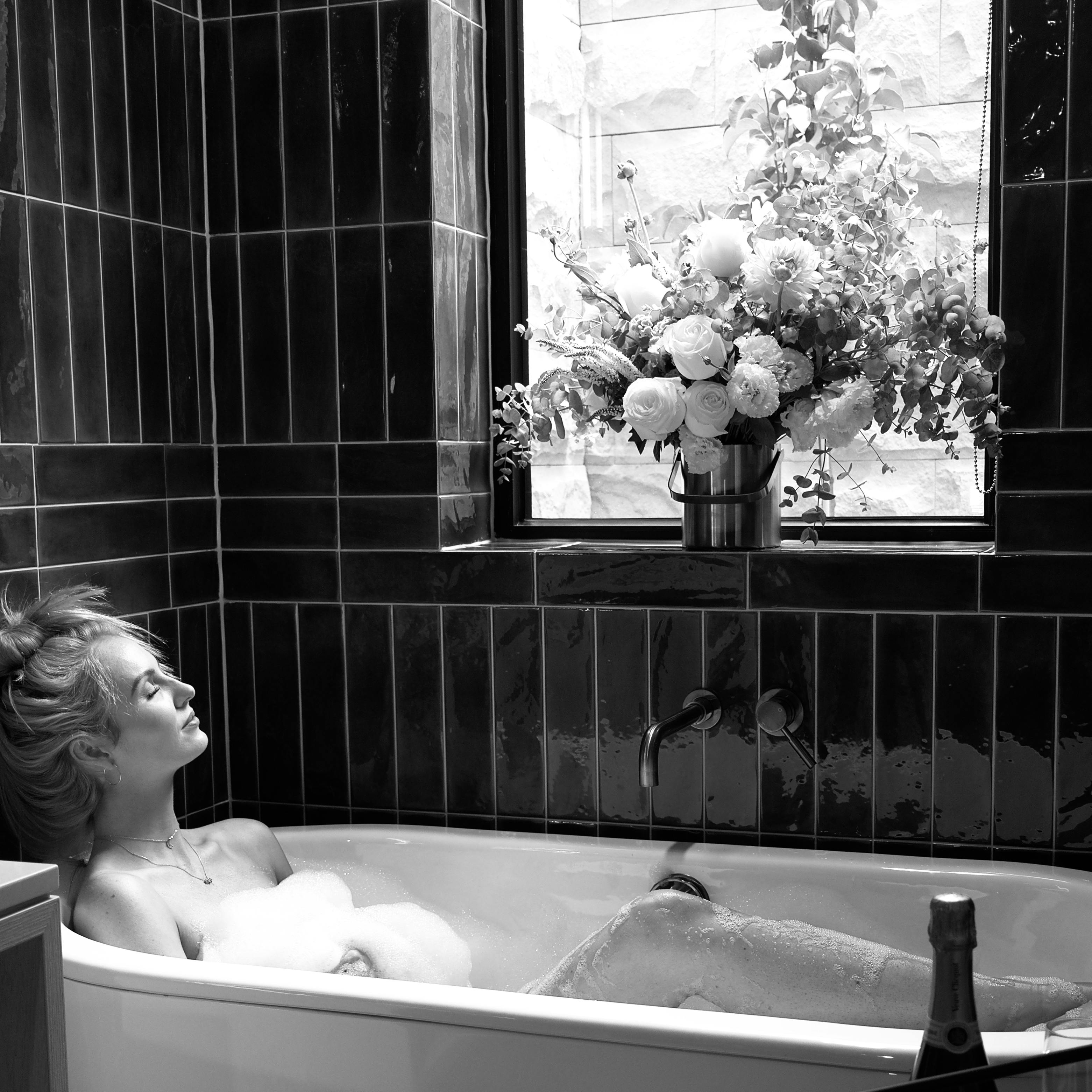 Black and white image of a woman enjoying a relaxing bath in a minimalist bathroom.
