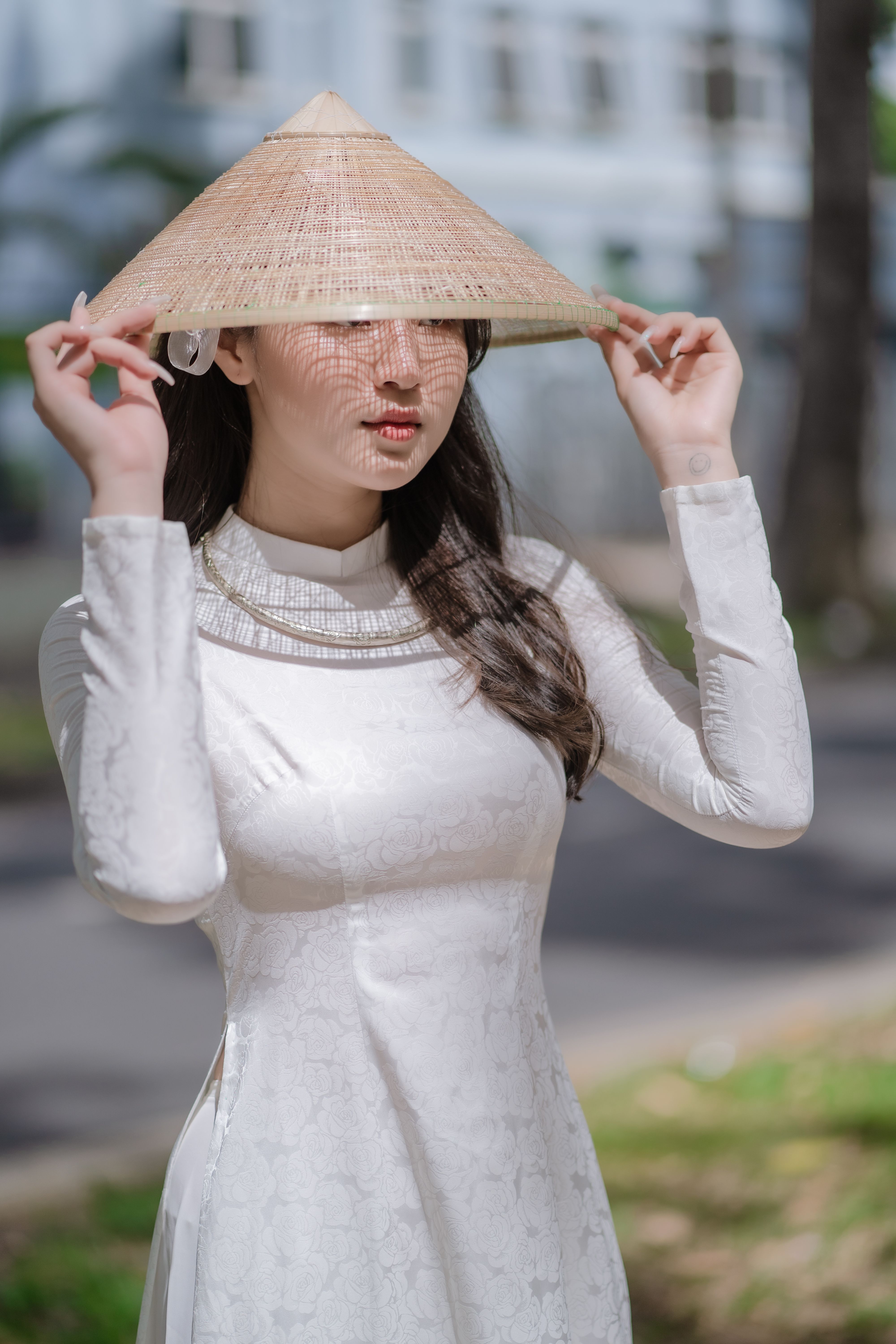 A woman wearing a traditional Vietnamese ao dai and conical hat poses outdoors in natural lighting.