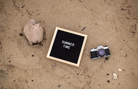 Flat lay of a vintage camera and summer sign on sandy beach setting a warm vacation mood.