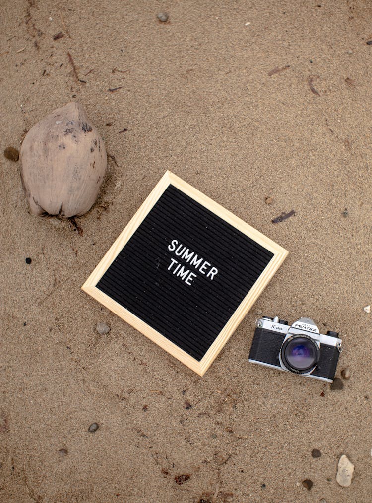 Board With Text 'Summer Time' Beside Cocoa Bean And Vintage Camera On The Beach