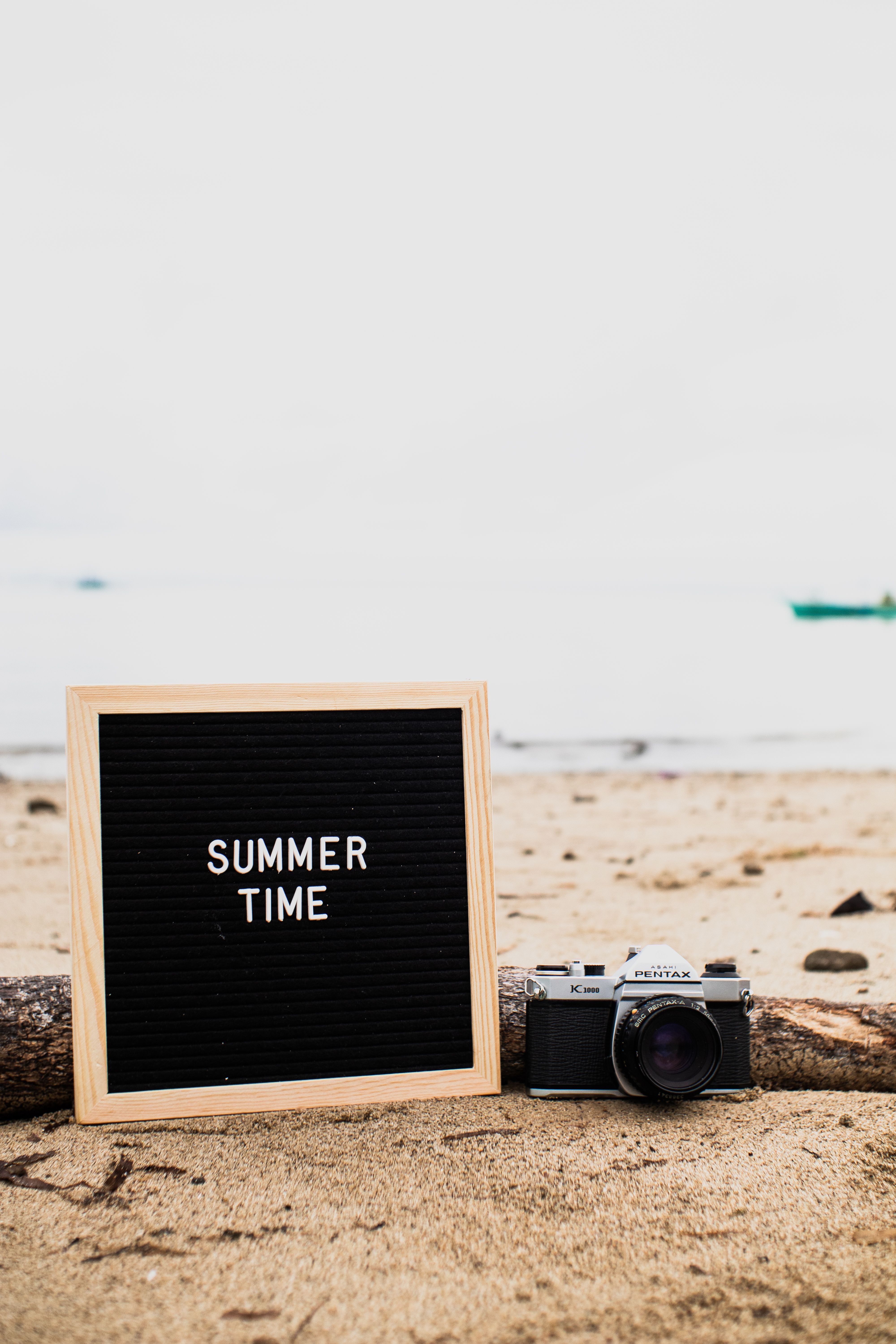 A vintage camera and summer sign on a sandy beach, perfect for travel inspiration.