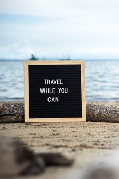 Motivational quote 'Travel While You Can' on a beach setting. Perfect for wanderlust inspirations.